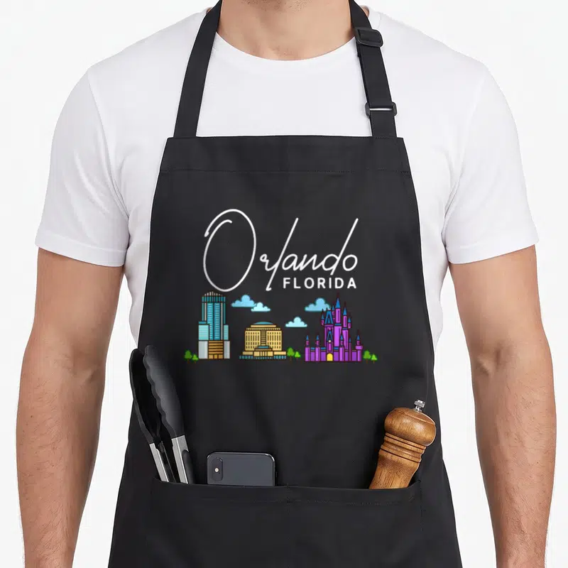 Orlando skyline florida apron - Cartoon Orlando Florida skyline with skyscraper, castle, clouds, and green trees — shown on a black cotton canvas apron against a white background