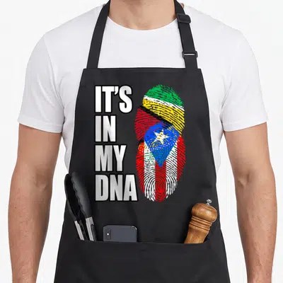 Guyanese heritage aprons - IT'S IN MY DNA text beside a fingerprint shaped like a Guyana and Puerto Rico flag composite — shown on a black cotton canvas apron against a white background
