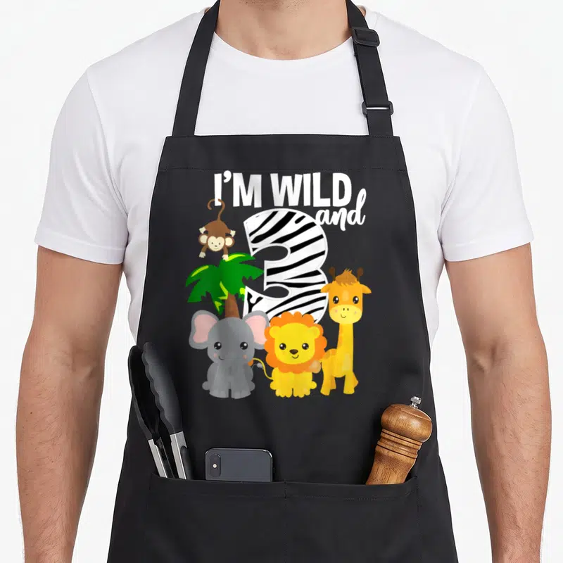 Zoo theme safari birthday apron - Zebra-striped number 3 with elephant lion giraffe monkey and palm tree under I'M WILD — shown on a black cotton canvas apron against a white background