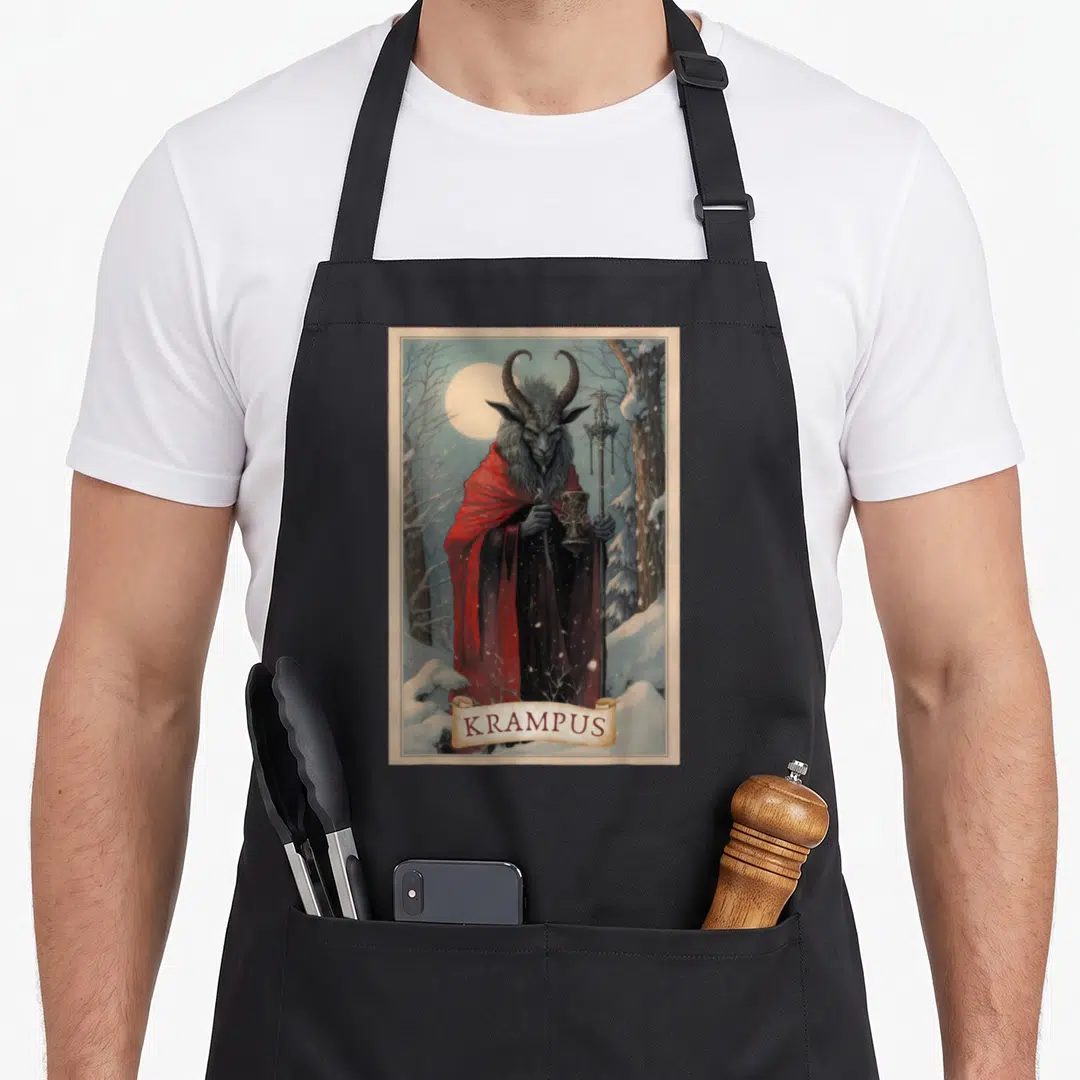Merry xmas apron - Krampus figure in red cloak holding goblet and staff in snowy forest with banner text — shown on a black cotton canvas apron against a white background