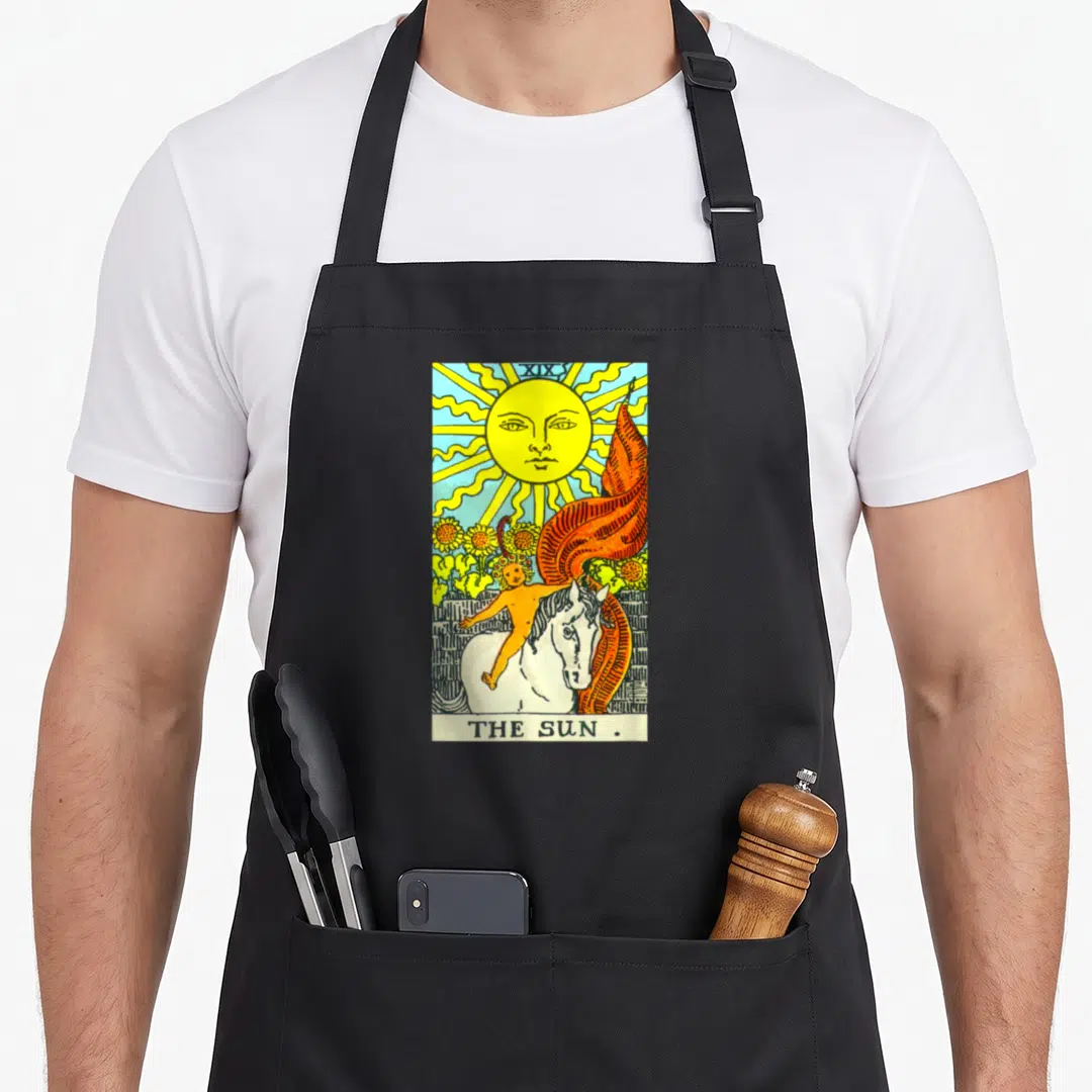 Sun tarot card apron - Yellow sun with face, child on white horse, sunflowers, orange banner, XIX and THE SUN text — shown on a black cotton canvas apron against a white background