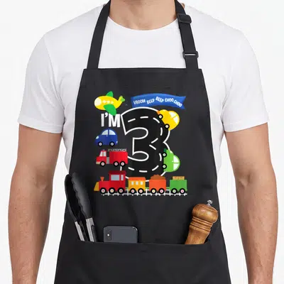 Airplane truck apron - Number 3 road design with airplane fire truck train and VROOM BEEP BEEP CHOO CHOO banner — shown on a black cotton canvas apron against a white background