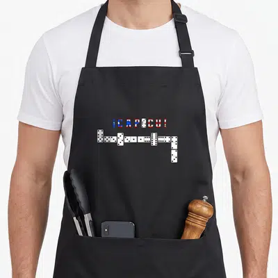 Player dominoes apron - I CAPICU text in flag colors above a row of dominoes turning down — shown on a black cotton canvas apron against a white background