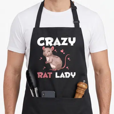 Rat pet animal apron - Cartoon brown rat with pink hearts and CRAZY RAT LADY text — shown on a black cotton canvas apron against a white background