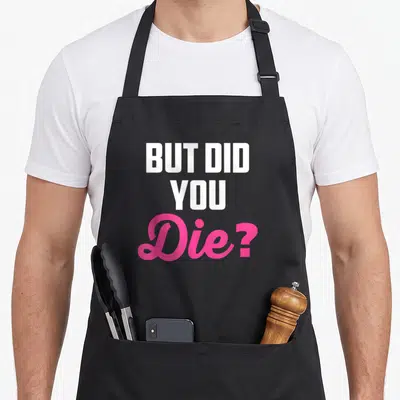 But nurse apron - Stacked white and pink text reading But Did You Die on black fabric — shown on a black cotton canvas apron against a white background