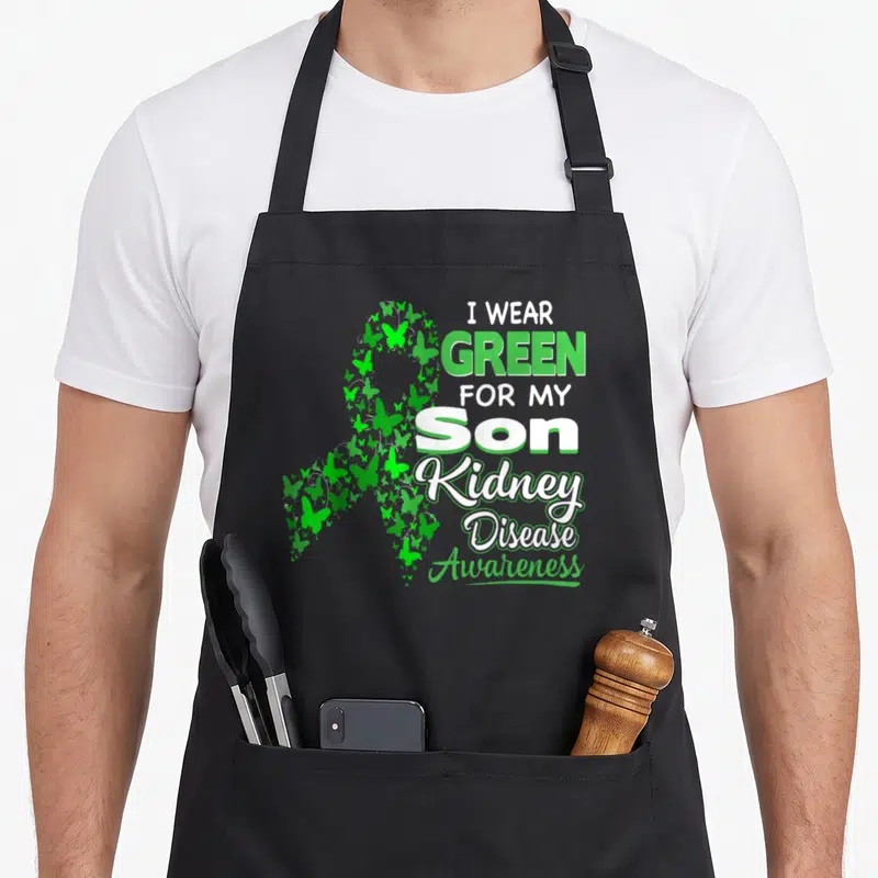 Son kidney disease awareness apron - Green and white awareness ribbon made of small butterflies next to stacked text — shown on a black cotton canvas apron against a white background
