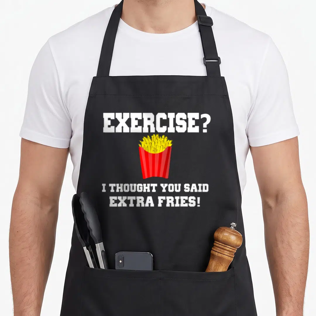 Fry an extra apron - White text reading exercise extra fries above a red container of yellow cartoon french fries — shown on a black cotton canvas apron against a white background