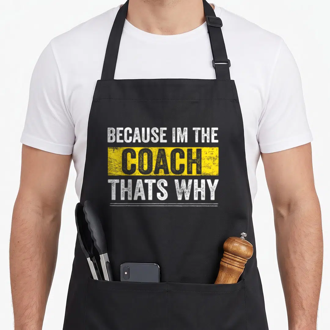 Retro coach apron - Stacked text Because Im The Coach That's Why in white and grey over yellow block — shown on a black cotton canvas apron against a white background