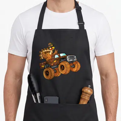 Thanksgiving truck aprons - Cartoon turkey in sunglasses driving brown monster truck with pumpkins and leaves — shown on a black cotton canvas apron against a white background
