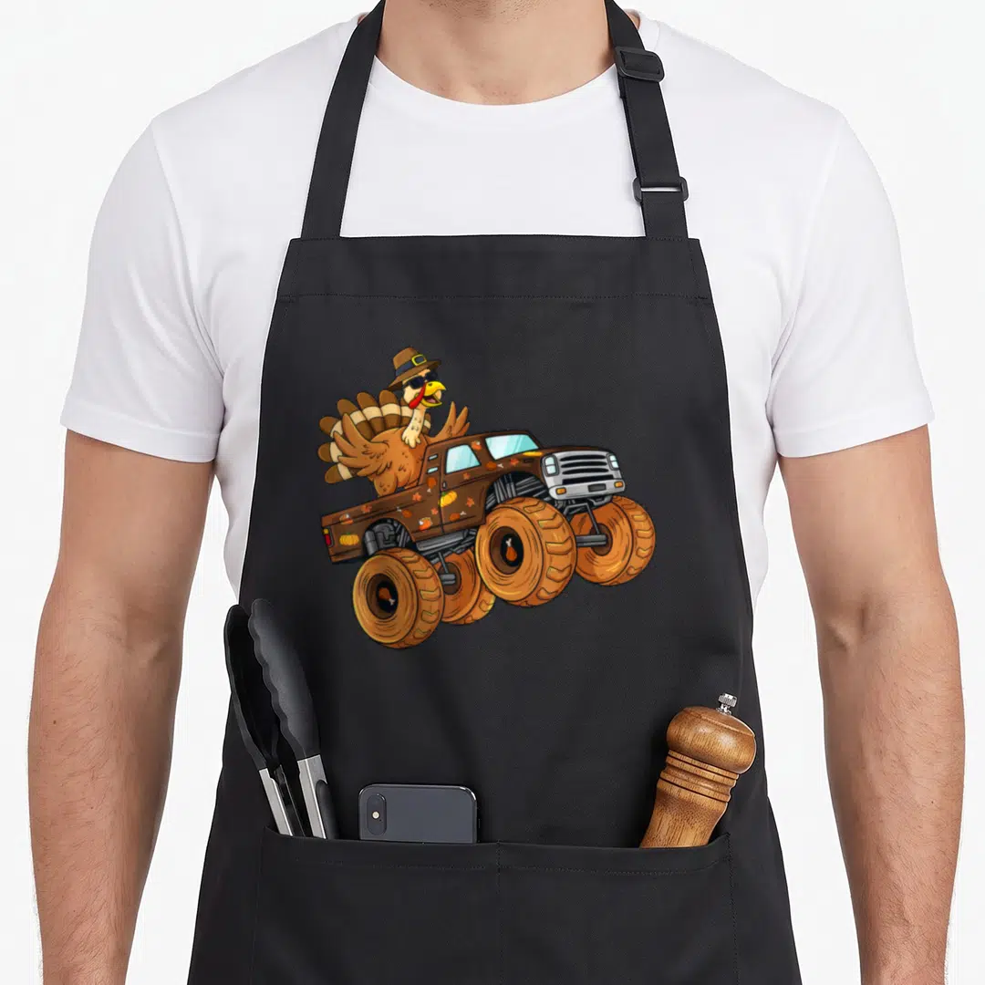 Thanksgiving truck aprons - Cartoon turkey in sunglasses driving brown monster truck with pumpkins and leaves — shown on a black cotton canvas apron against a white background