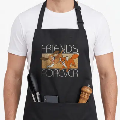 Hound fox print apron - FRIENDS FOREVER text with cartoon dog and fox jumping over tan dotted rectangle — shown on a black cotton canvas apron against a white background