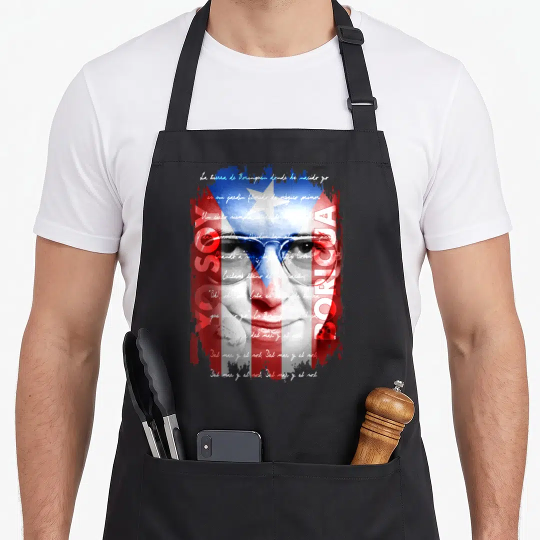 Hector soy apron - Woman face overlaid with Puerto Rican flag and Spanish lyrics in red white blue — shown on a black cotton canvas apron against a white background