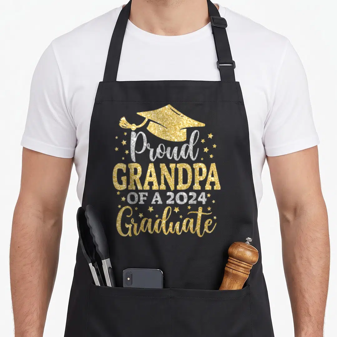 Senior grandpa apron - Gold glitter graduation cap with Proud Grandpa Of A 2024 Graduate text and small stars — shown on a black cotton canvas apron against a white background