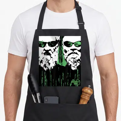Plato matrix apron - Two stylized faces over green rain with The Philosopher's Shirt text — shown on a black cotton canvas apron against a white background