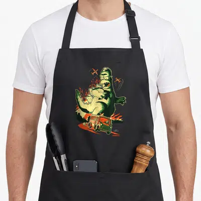 Treehouse horror apron - Large green monster holding smaller monster with two orange planes and a bus in cartoon style — shown on a black cotton canvas apron against a white background
