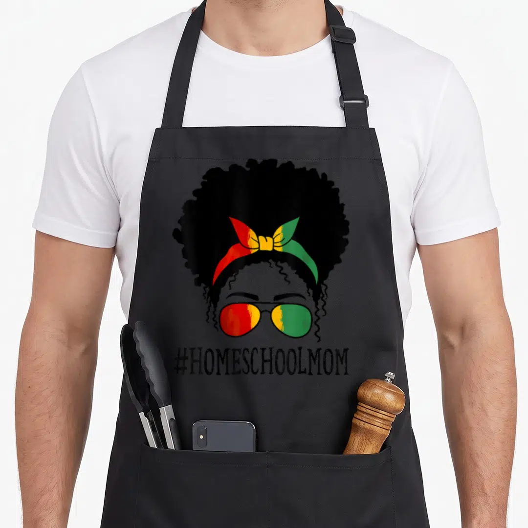 Homeschool messy aprons - Cartoon woman with afro, sunglasses, and #HOMESCHOOLMOM text in red yellow green — shown on a black cotton canvas apron against a white background