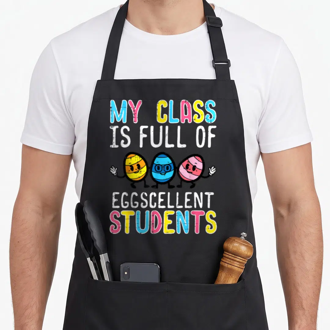 Eggcellent teacher apron - Three cartoon eggs holding hands under MY CLASS IS FULL OF EGGSCELLENT STUDENTS text — shown on a black cotton canvas apron against a white background