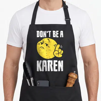 Karen internet meme apron - Yellow emoji giving middle finger between white DON'T BE A KAREN text — shown on a black cotton canvas apron against a white background