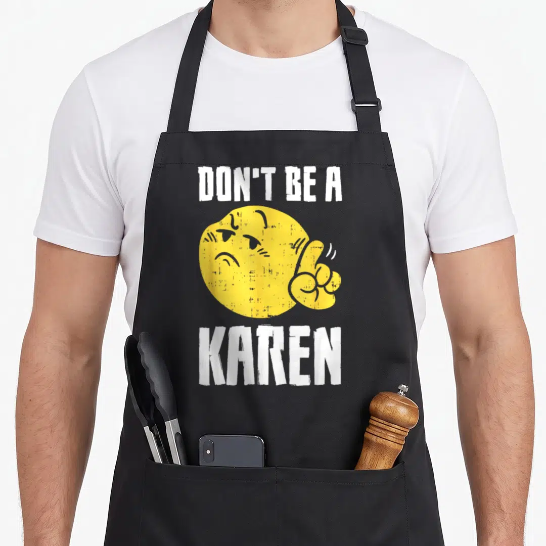 Karen internet meme apron - Yellow emoji giving middle finger between white DON'T BE A KAREN text — shown on a black cotton canvas apron against a white background