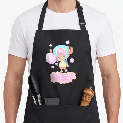 Tony anime apron - Chopper holding pink cotton candy with Japanese text below in cartoon style — shown on a black cotton canvas apron against a white background