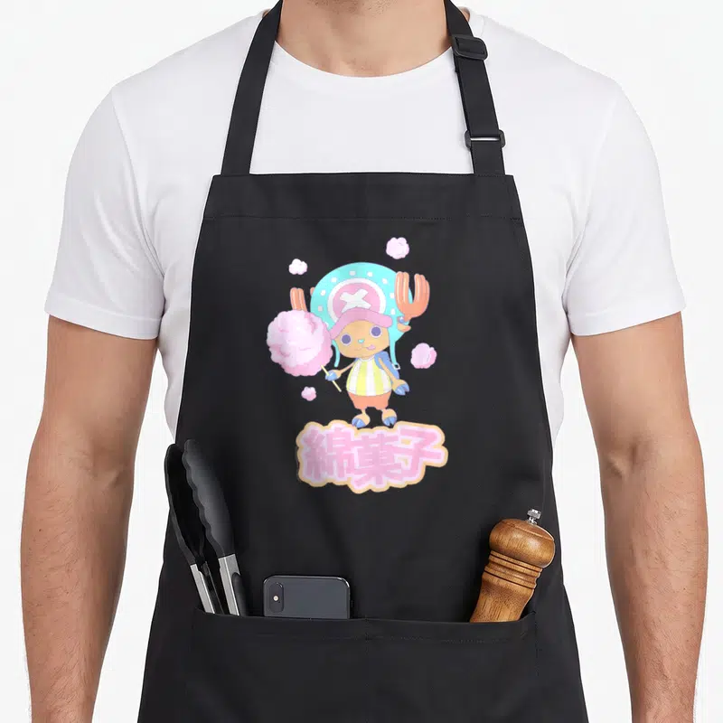 Tony anime apron - Chopper holding pink cotton candy with Japanese text below in cartoon style — shown on a black cotton canvas apron against a white background