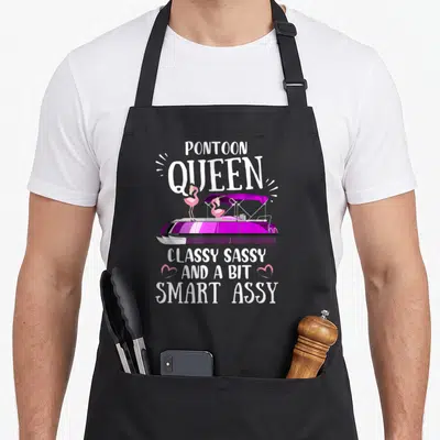 Pontoon smart apron - Purple pontoon boat with two pink flamingos and white sarcastic text flanked by hearts — shown on a black cotton canvas apron against a white background