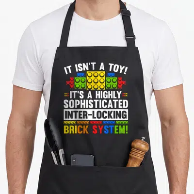 Brick grill master apron - Sarcasm text IT ISN'T A TOY above and below colorful interlocking toy bricks — shown on a black cotton canvas apron against a white background