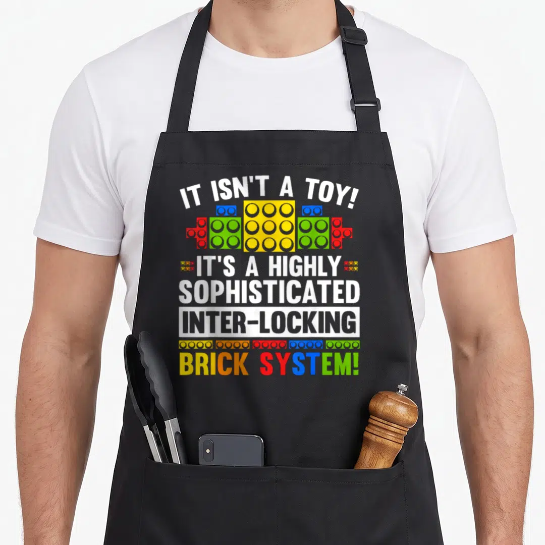 Brick grill master apron - Sarcasm text IT ISN'T A TOY above and below colorful interlocking toy bricks — shown on a black cotton canvas apron against a white background