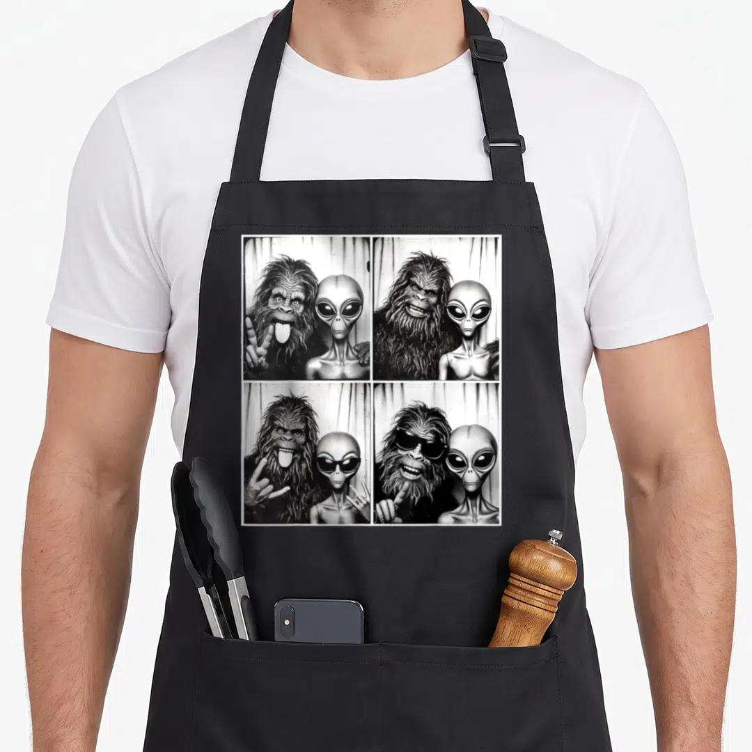 Photobooth bigfoot apron - Four-panel black white grey photo grid of Bigfoot and Alien posing together — shown on a black cotton canvas apron against a white background