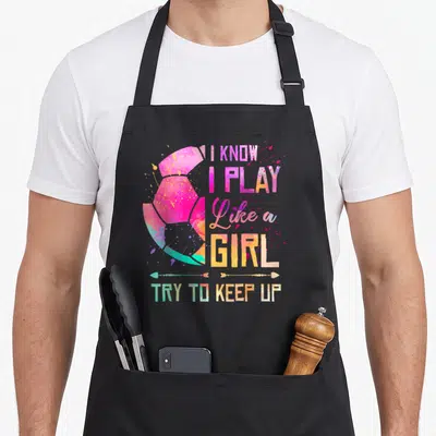 Play soccer apron - Watercolor soccer ball with stacked text I KNOW I PLAY Like a GIRL TRY TO KEEP UP and two arrows — shown on a black cotton canvas apron against a white background