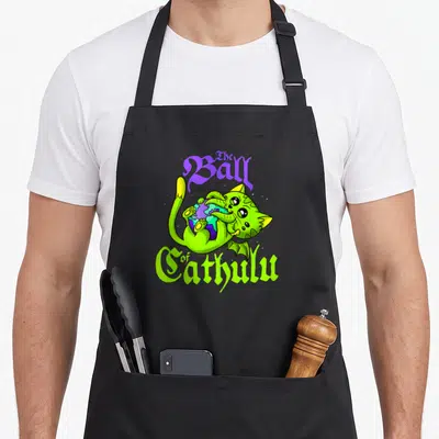 Eating kawaii apron - Lime green cartoon cat hugging purple and blue earth under gothic text — shown on a black cotton canvas apron against a white background