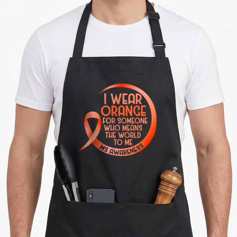 Someone msemen apron - Orange awareness ribbon overlapping a circular arc with stacked text reading I Wear Orange — shown on a black cotton canvas apron against a white background