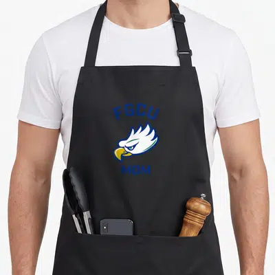Fgcu arched eagles apron - Cartoon eagle head with blue FGCU text above and MOM text below — shown on a black cotton canvas apron against a white background