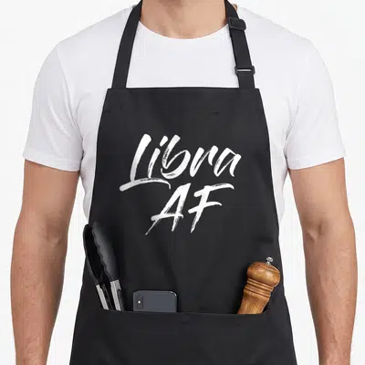 Funny libra apron - White brush script text reading Libra AF on grey background — shown on a black cotton canvas apron against a white background