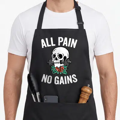 Gym round neck apron - Skull biting barbell with red rose and ALL PAIN NO GAINS text — shown on a black cotton canvas apron against a white background