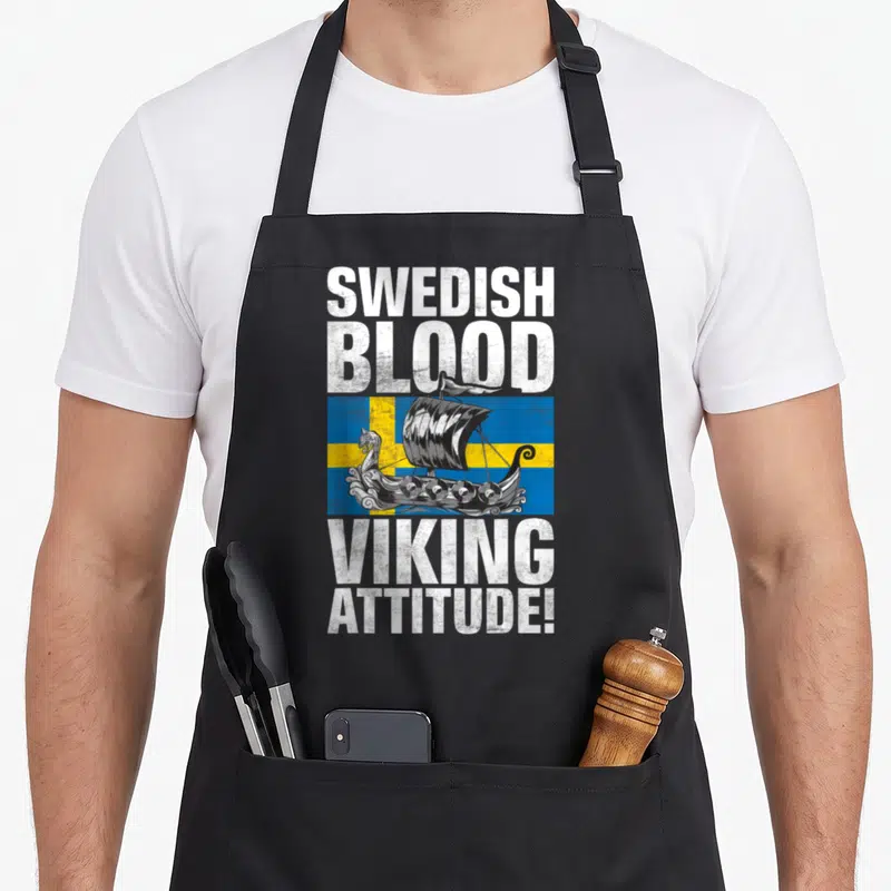 Blood swedish apron - Viking ship on Swedish flag with stacked SWEDISH BLOOD VIKING ATTITUDE text in distressed white — shown on a black cotton canvas apron against a white background