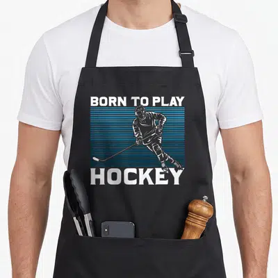 Goalie ice hockey apron - BORN TO PLAY HOCKEY text with white player silhouette over blue stripes — shown on a black cotton canvas apron against a white background