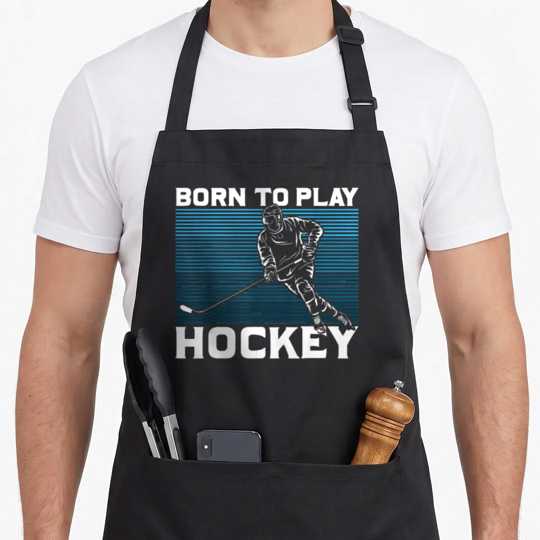 Goalie ice hockey apron - BORN TO PLAY HOCKEY text with white player silhouette over blue stripes — shown on a black cotton canvas apron against a white background