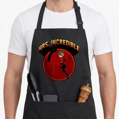 Incredible mrs apron - Elastigirl in red circle with MRS. INCREDIBLE text arching above in cartoon style — shown on a black cotton canvas apron against a white background