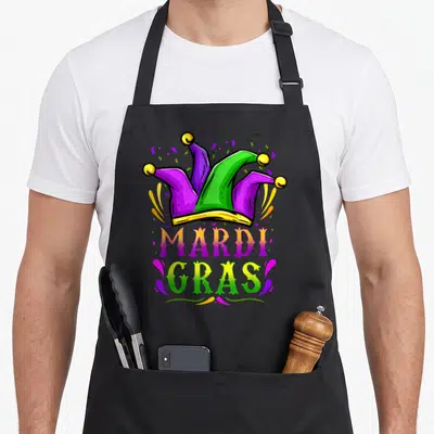 Hat carnival apron - Cartoon jester hat in purple green and yellow with MARDI GRAS text and confetti swirls — shown on a black cotton canvas apron against a white background