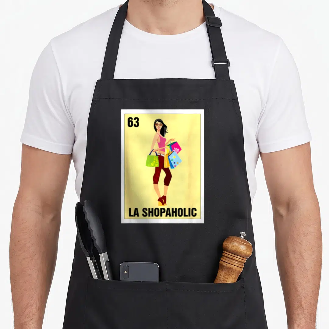 Shopaholic bingo aprons - Yellow bingo card with 63 and LA SHOPAHOLIC text showing a woman holding colorful shopping — shown on a black cotton canvas apron against a white background