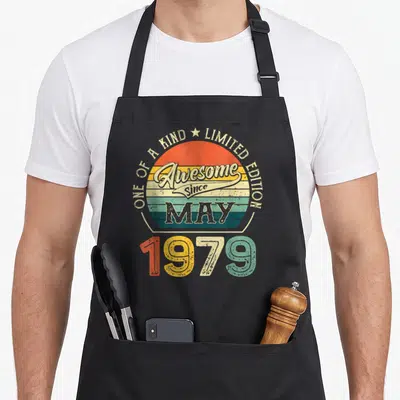 May born day apron - Retro sun graphic with One of a Kind Limited Edition text and colorful 1979 numbers — shown on a black cotton canvas apron against a white background