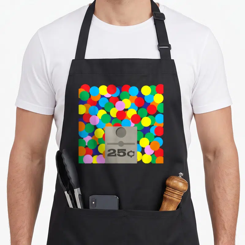 Gum machine apron - Grey 25c vending slot centered on a background of scattered red, blue, yellow, green, and pink — shown on a black cotton canvas apron against a white background