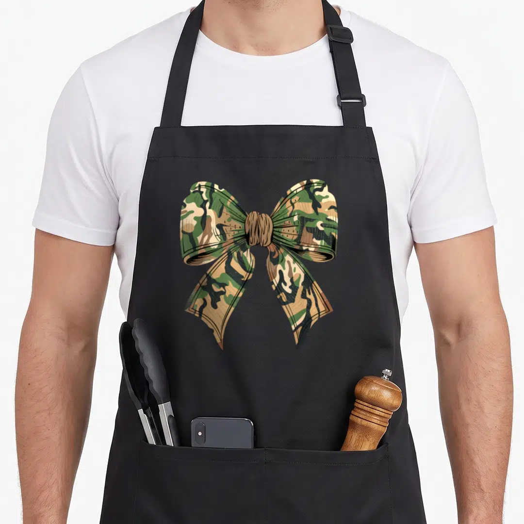 Coquette camo apron - Realistic bow filled with green brown and tan camouflage pattern — shown on a black cotton canvas apron against a white background