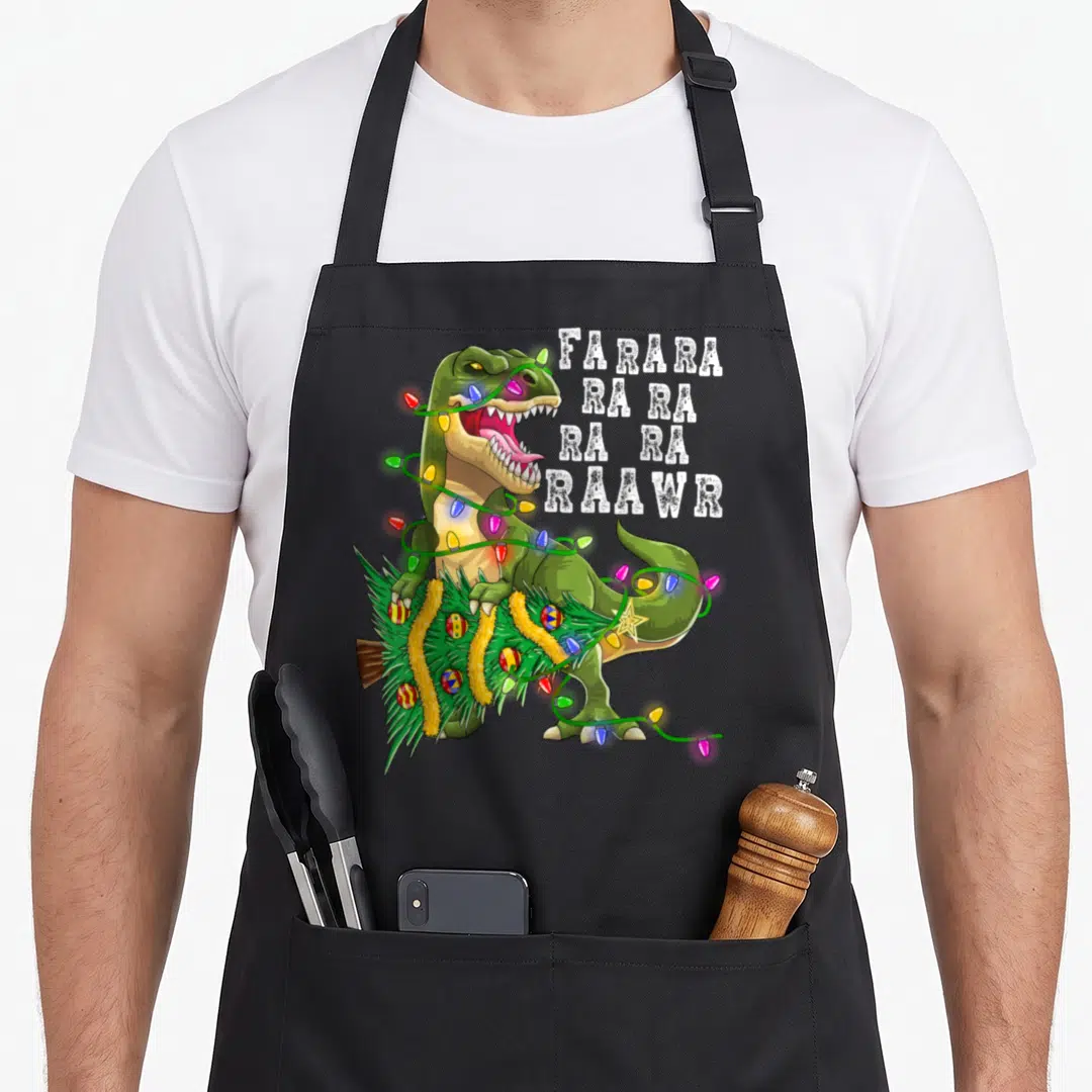 Dinosaur christmas tree apron - Green T-Rex holding Christmas tree wrapped in multi-colored lights with stacked white — shown on a black cotton canvas apron against a white background