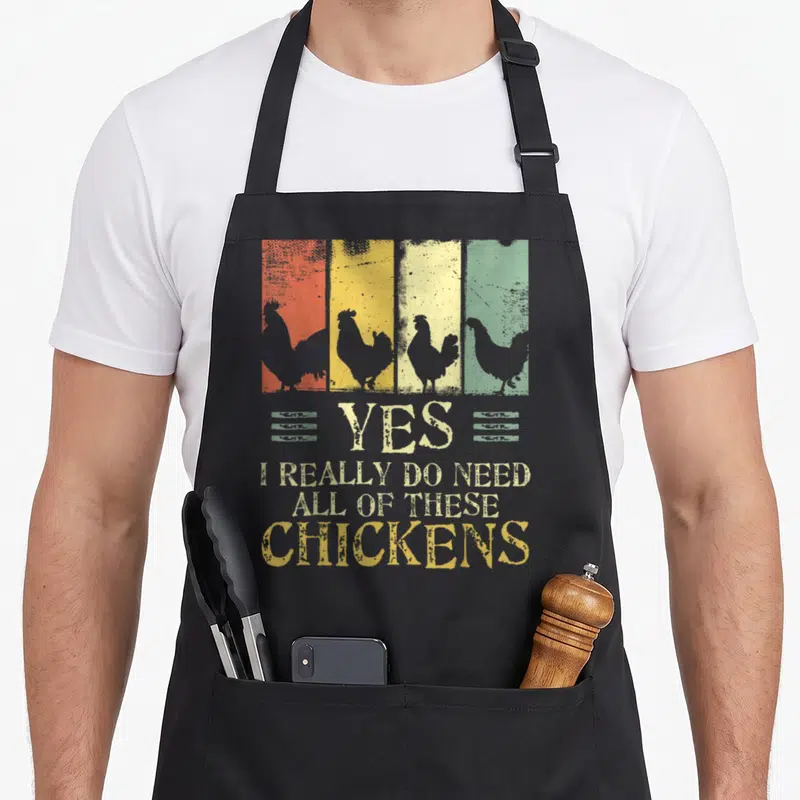 These chicken apron - Four striped panels with chicken silhouettes and stacked distressed text reading Yes I Really Do — shown on a black cotton canvas apron against a white background