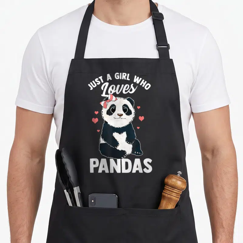 Panda kawaii apron - Cartoon panda with pink bow and hearts surrounded by JUST A GIRL WHO Loves PANDAS text — shown on a black cotton canvas apron against a white background