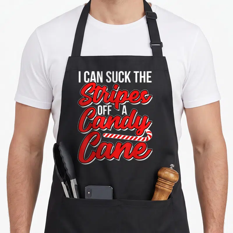 Suck candy cane apron - Red and white stacked text reading I Can Suck the Stripes Off a Candy Cane with small — shown on a black cotton canvas apron against a white background