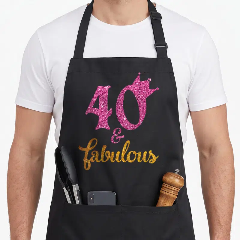 Celebration fabulous birthday apron - Pink glitter 40 with crown and gold fabulous script — shown on a black cotton canvas apron against a white background
