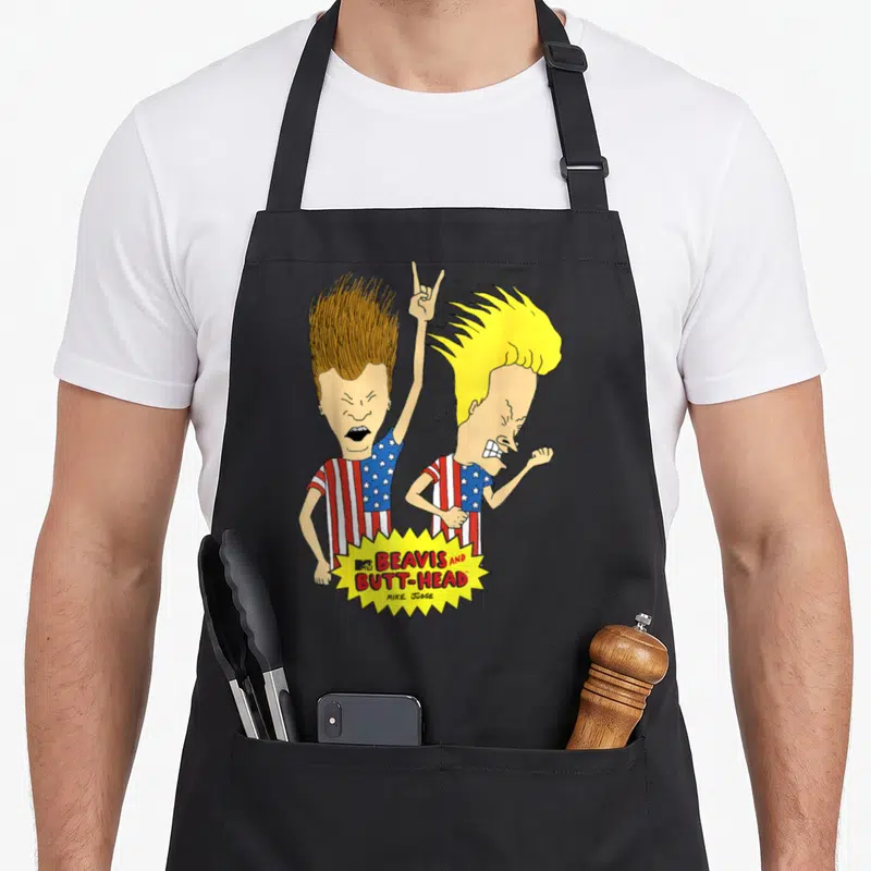 Beavis us aprons - Two cartoons in flag shirts with yellow burst logo reading Beavis and Butt-Head Mike Judge — shown on a black cotton canvas apron against a white background